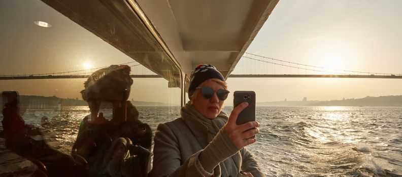 Young amazing woman outdoors on boat in sea take a selfie by mobile phone. Spring