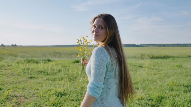 Russian young girl with a bouquet of flowers in hands posing on a warm summer evening in the field