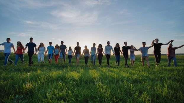 Silhouettes of nineteen friends holding hands on a sunset background