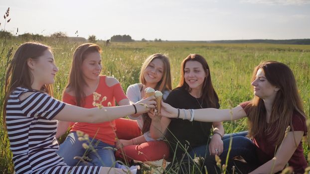 Five young schoolgirls are eating ice cream on a meadow joining hands with ice cream