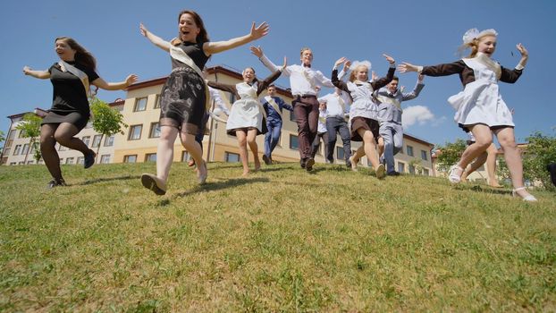 Happy graduates of the Russian school appear from behind the hill and run towards happiness