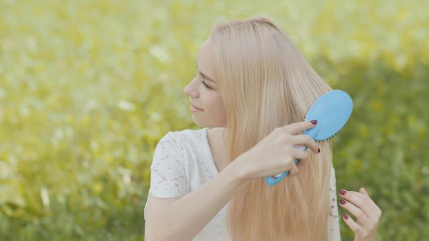 Russian young blonde girl is combed sitting on the grass in the park