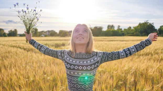 A sixteen year old teen girl with flowers of cornflowers is spinning in a field