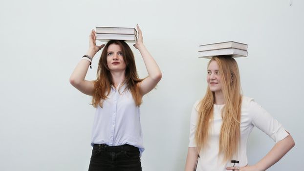 Two schoolgirls play with books holding them on their heads