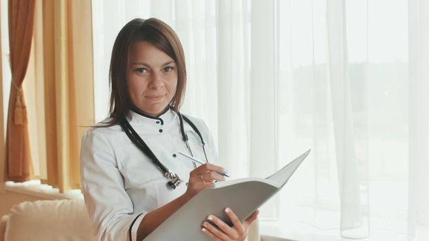 A young woman doctor writes in a summary in a good mood