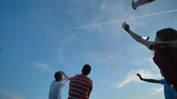 Young guys and a girl are waving their hands at the airplane in the sky