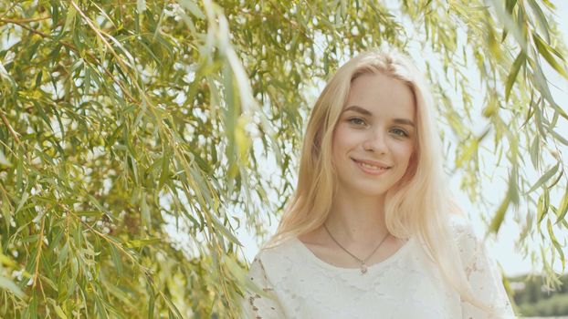 Young Russian girl blonde posing against a background of willow tree branches.