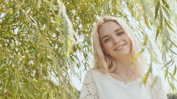 Young Russian girl blonde posing against a background of willow tree branches.