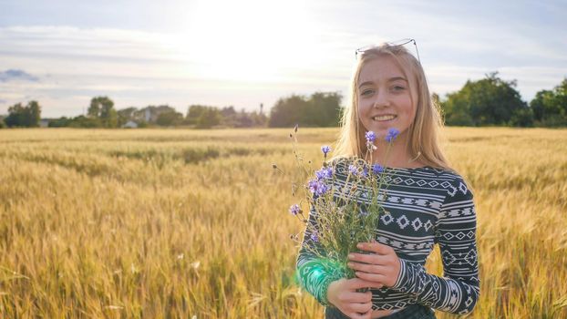 Sixteen year old girl teenager with flowers of cornflowers posing in a wheat field