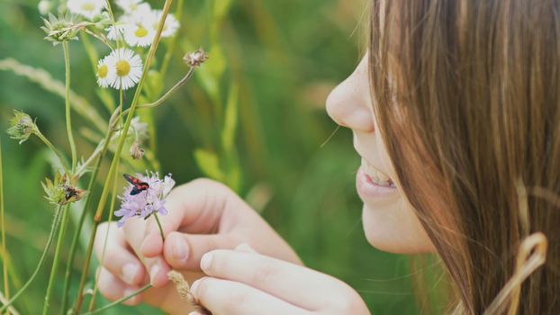 Teenage girl admires a moth on a flower. Warm summer day