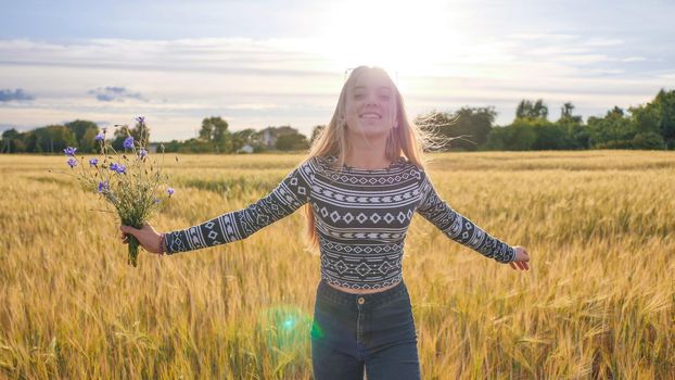 A sixteen year old teen girl with flowers of cornflowers is spinning in a field