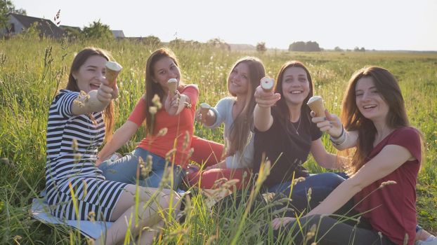 Five young schoolgirls eat and demonstrate ice cream on the meadow on a warm summer day