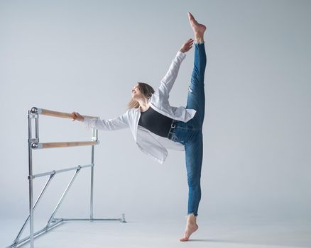 Caucasian woman in casual clothes pulls the split at the ballet barre