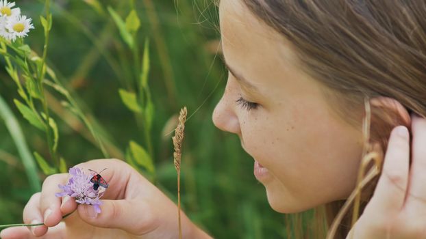 Teenage girl admires a moth on a flower. Warm summer day