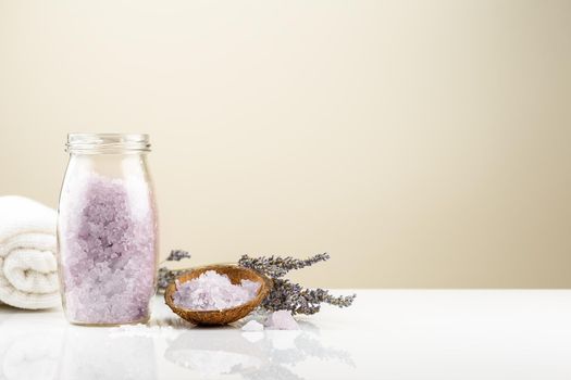 Lavender bath salt in a glass jar with bunch of dry lavender flowers and white towel