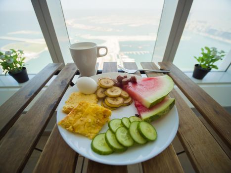 Light breakfast with scrambled eggs and fruit on the background of a skyscraper window on Palm Jumeirah. Dubai