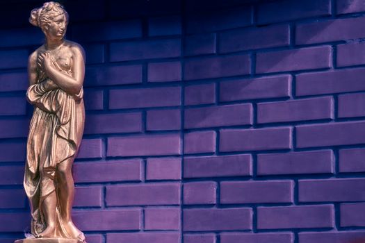 a carved or cast figure of a person or animal, especially one that is life-size or larger.Golden bronze statue of an antique woman and matte lilac background with space for text.