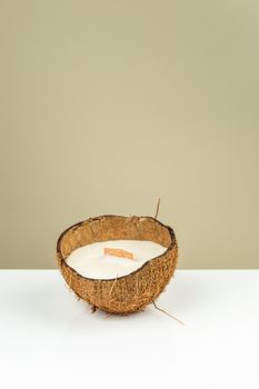 Decorative natural soy wax candle in a coconut shell with wooden candle wick on white glossy surfase. Reuse DIY idea