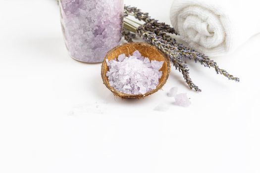 Lavender bath salt in a coconut shell bowl with bunch of dry lavender flowers and white towel