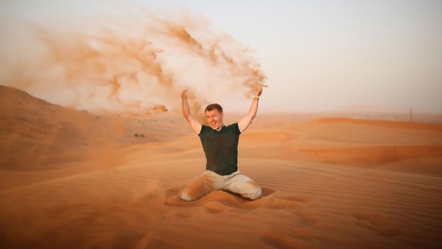 The guy throws sand over himself in the desert. The desert is next to Dubai. UAE