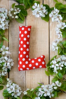 Natural wooden background with white flowers fruit tree. In the middle is the letter L, is made of red polka dot fabric.