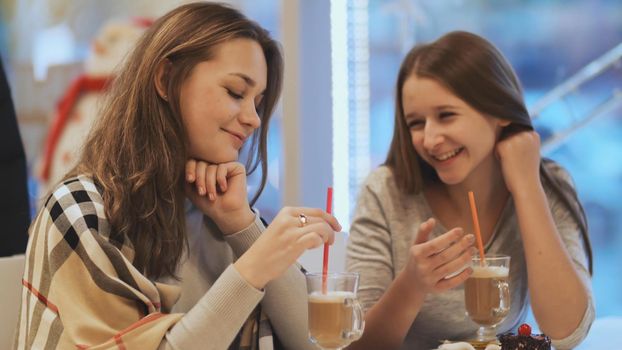 Two schoolgirls girlfriends drinking cocktails and talking in a cafe fun. Autumn, Winter