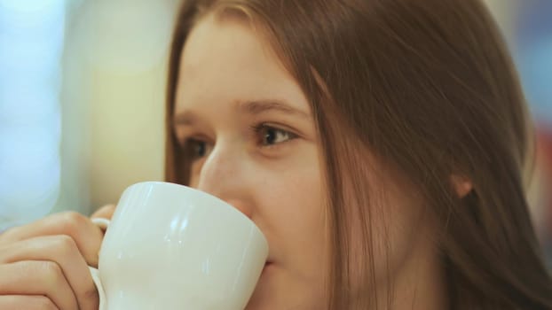 Close-up face of young beautiful schoolgirl, drinking coffee from a cup