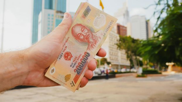 Man recounts Vietnamese money. Two hundred and one hundred thousandth of the banknote on the background of downtown Ho Chi Minh city