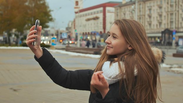 Young beautiful girl in jacket does selfi autumn in one of the city streets