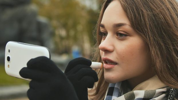 The young beautiful girl paints her lips with lipstick hygienic autumn time. Close up