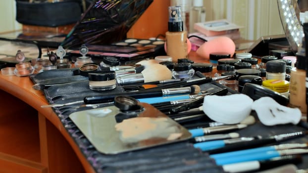 The make-up worker's desk. Many cosmetics are scattered on the table. The make-up artist paints the model