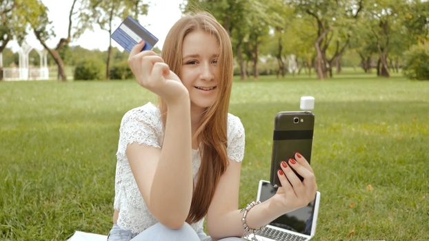 A young girl makes a payment in an online bank using a mini magnetic mobile card reader