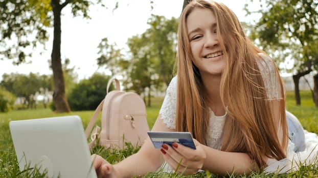 Pretty young student girl makes purchases online using a credit card and laptop computer