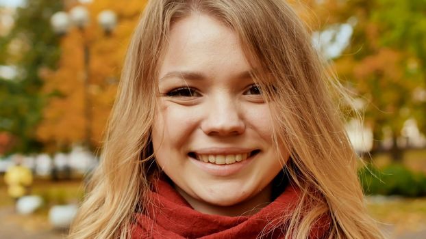 Face of young attractive girl close-up. Smiling girl posing on camera among colorful autumn park trees