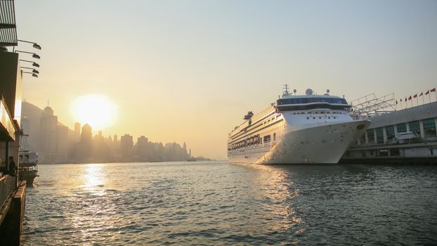 Cruise liner in Victoria harbor in the rays of sunset. View of the sea of Hong Kong and skyscrapers against the backdrop of the mountains