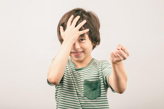 White 6 years old boy covering his head threatens the enemy with a fist looking to the camera. Kid quarreling and fighting. Child abuse concept