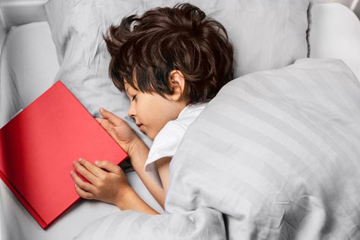 Child sleeping at night in his bed with a red story book. Kids literature concept. Reading before bed for children