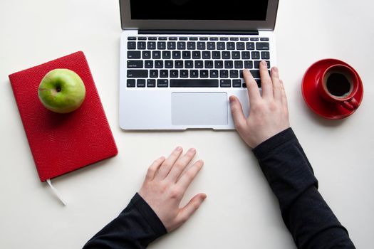 Man hands on wireless keyboard with red notebook, green apple and red cup of coffee on white table