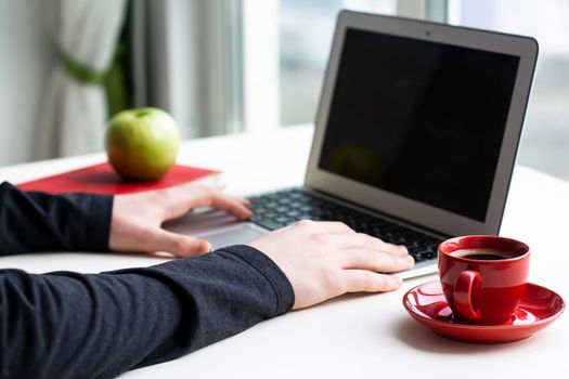 Man hands on wireless keyboard with red notebook, green apple and red cup of coffee on white table