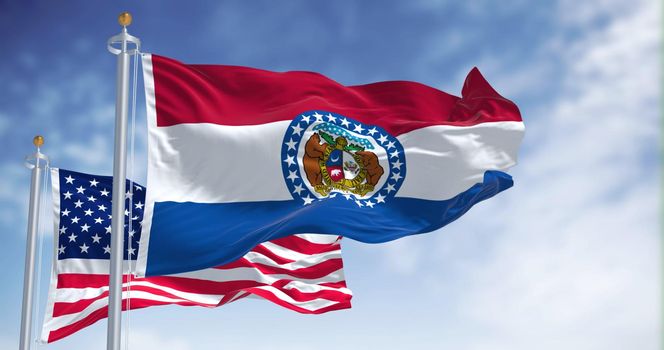 The Missouri state flag waving along with the national flag of the United States of America. In the background there is a clear sky. Missouri is a state in the Midwestern region of the United States