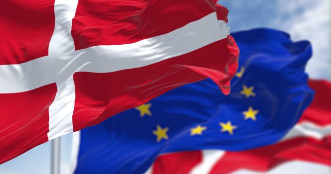 Detail of the national flag of Denmark waving in the wind with blurred european union flag in the background on a clear day. Democracy and politics. European country. Selective focus.