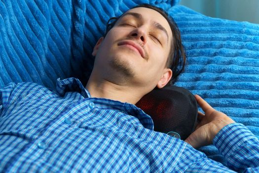 Electric massage cushion with infrared warming areas. Milineal man relaxes at home