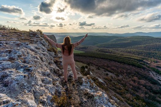 The girl at sunset. The girl stands with her back on the top of the mountain and looks at the sunset, welcomes the sun with her hands up, in Hampi. Meditation, alone with nature, silence. Hands up