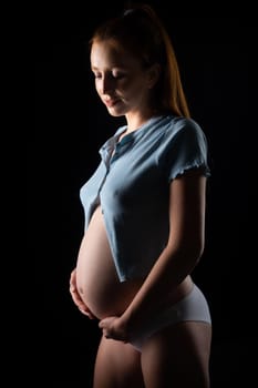 A pregnant woman with a big belly and red hair. Posing on a black background in the studio.