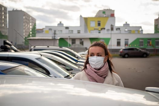 picture of a girl in a mask, on the street. Against the background of parked cars. isolated Covid-19 pandemic.