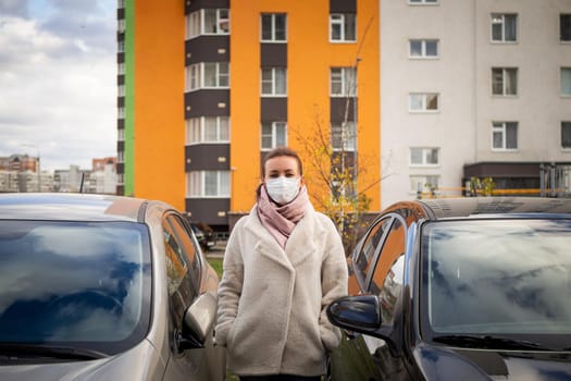 picture of a girl in a mask, on the street. Against the background of parked cars. isolated Covid-19 pandemic.
