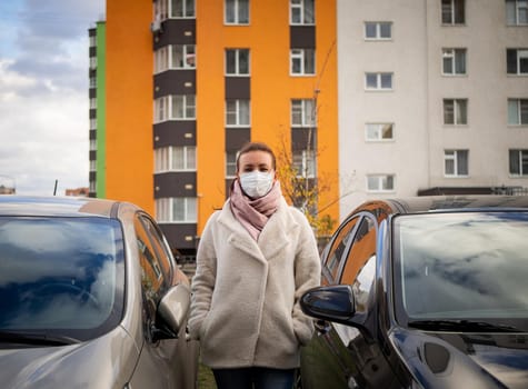 picture of a girl in a mask, on the street. Against the background of parked cars. isolated Covid-19 pandemic.