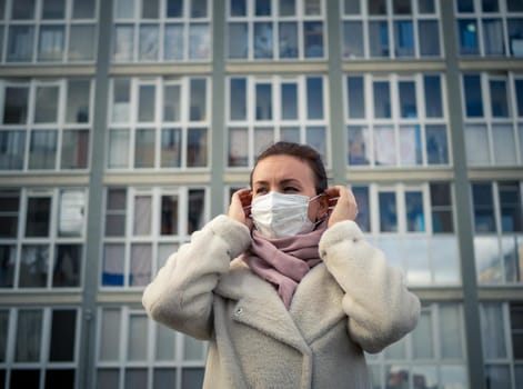 Shot of a girl in wearing face mask for protection, on the street. Against the background of a residential building with windows. lockdown Covid-19 pandemic.