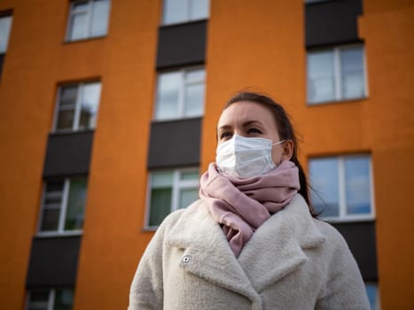 Shot of a girl in wearing face mask for protection, on the street. Against the background of a residential building with windows. lockdown Covid-19 pandemic.