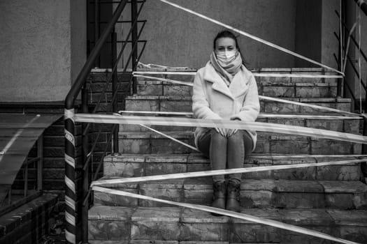 Photo of a girl in a mask. Sitting on the street with danger warning tapes. isolated Covid-19 pandemic.